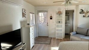 A bedroom with a bed, a TV, a dresser, a ceiling fan, and a door leading to a bathroom.