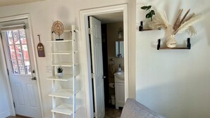 A living room with a grey sofa, a white shelving unit, and a door leading to a bathroom.