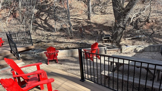 A wooden deck with red Adirondack chairs and a black metal railing.