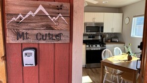 A wooden sign with a mountain design and the text "Mt. Cutler" on a red door, a Master Lock on the door, and a kitchen with white cabinets, a microwave, and a stove.