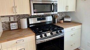A modern kitchen with stainless steel appliances, a wooden countertop, and white cabinetry.