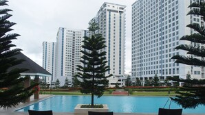 A pool area with lounge chairs and a lifebuoy, surrounded by tall residential buildings. - Modern Country Family Suite w/ Stunning Taal View (Tagaytay)