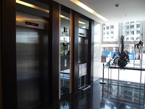 Un espace d’ascenseur moderne doté d’un écran numérique, d’un avis concernant la maintenance et offrant une vue sur l’extérieur grâce à de grandes fenêtres.