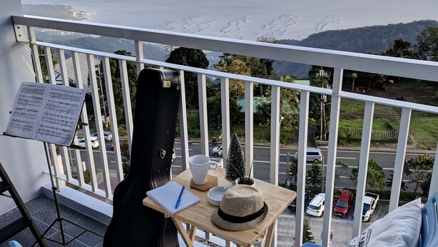 A balcony with a guitar, a music stand, and a small table with a hat and a cup. There are two blue chairs with white cushions. - Modern Country Family Suite w/ Stunning Taal View (Tagaytay)