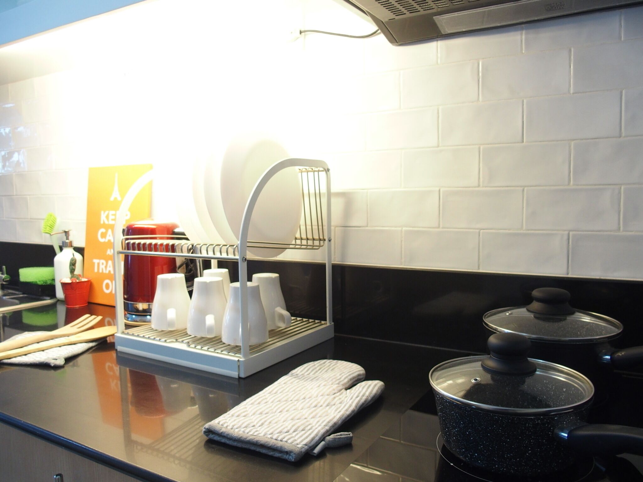 Un comptoir de cuisine avec un égouttoir, une bouilloire, une casserole et un panneau.