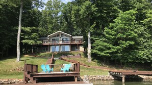 Un chalet au bord du lac, doté d’une terrasse, de meubles de jardin et d’un quai s’avançant dans l’eau.
