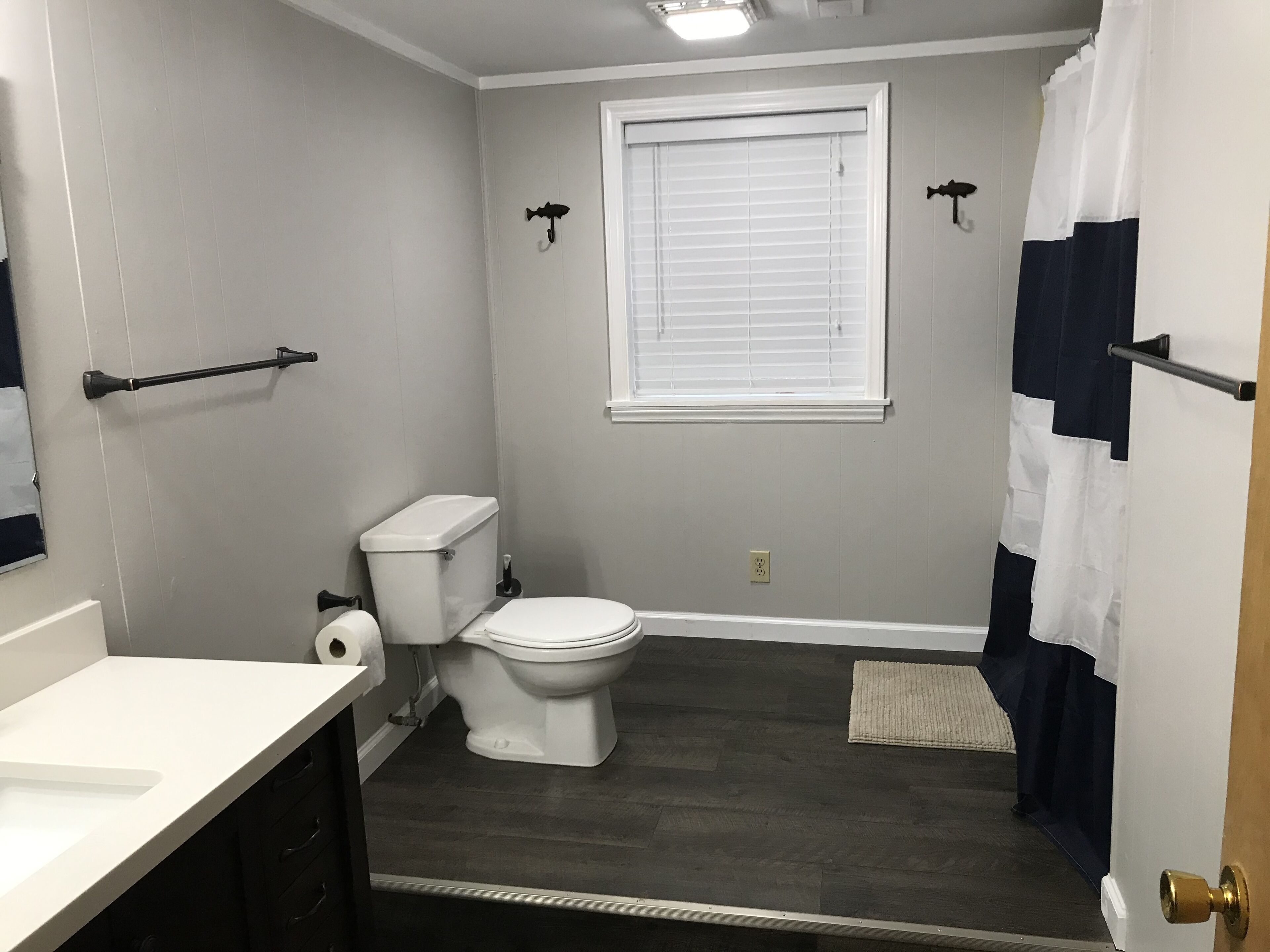 Une salle de bain comprenant des toilettes, un lavabo, une fenêtre avec des stores et un rideau de douche.