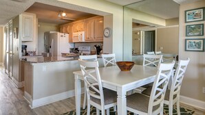 Una cocina con armarios blancos, una isla central y un comedor con sillas y mesa blancos.