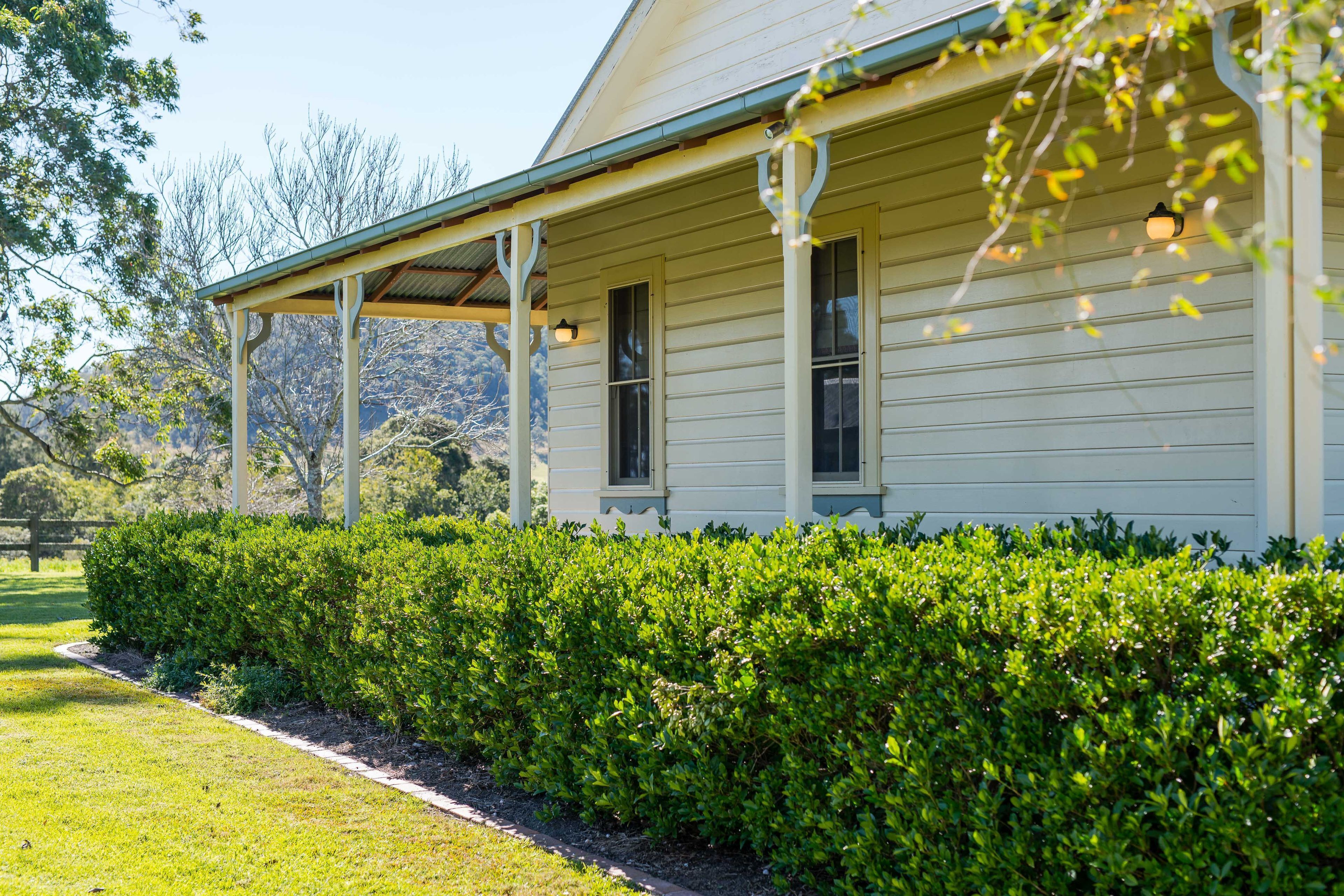 A white building with a covered porch and a well-maintained hedge in front.