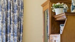 Una stanza con un armadio in legno, una tenda decorata, una sedia con un cuscino e un vaso con fiori.