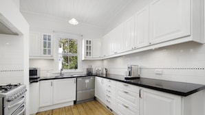 A modern kitchen with white cabinets, black countertops, stainless steel appliances, and a wooden floor. - Poet's Cottage 1912 Clifftop Walks, Fire, Spa Bath (Wentworth Falls)