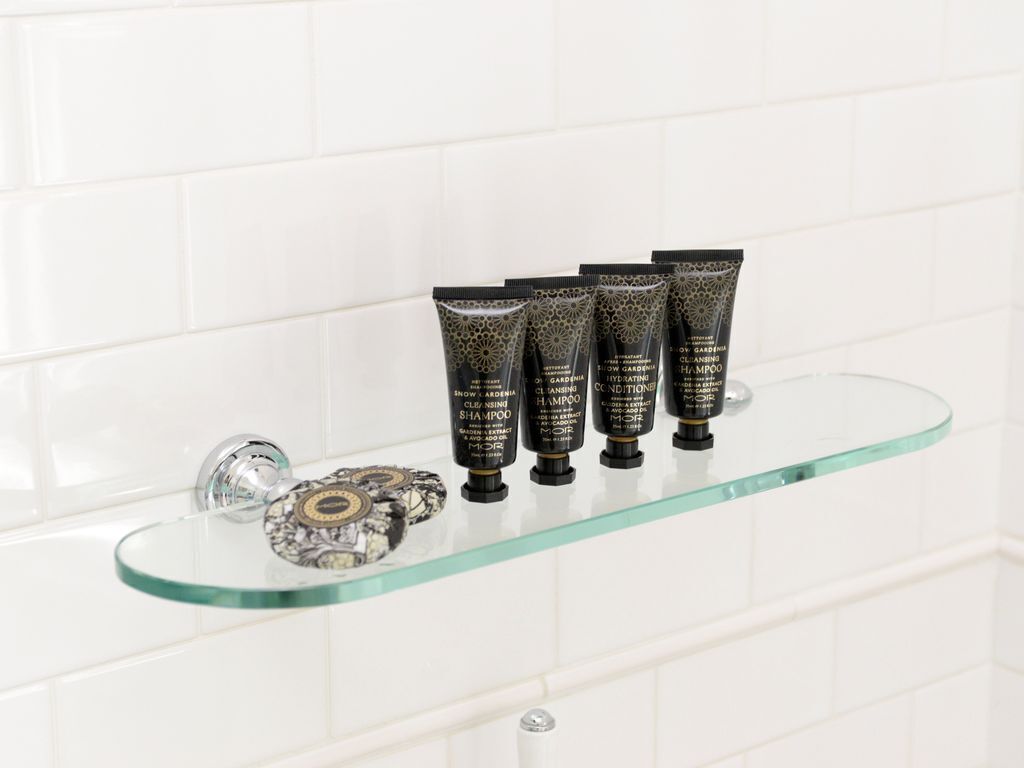A bathroom with a glass shelf holding four black tubes of shampoo and conditioner.