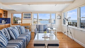 A spacious living area with a large window overlooking a body of water, a striped sofa, a coffee table, and a tripod.