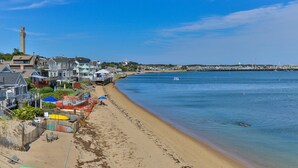 A coastal town with a sandy beach, a pier extending into the water, and a prominent tower in the background.
