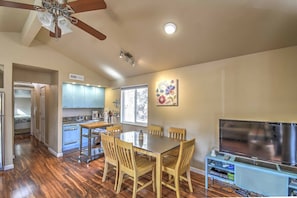 Una cocina amplia con armarios de madera, una mesa de comedor con sillas, un televisor de pantalla plana grande y un ventilador de techo.