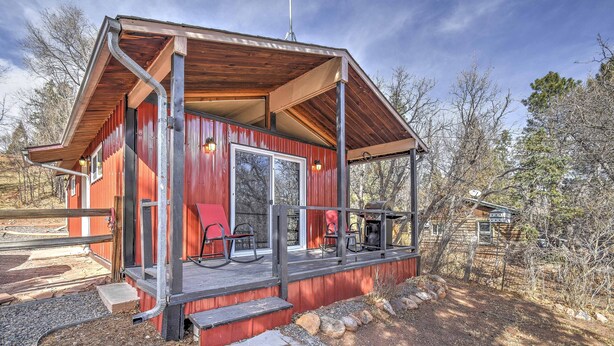 Eine rote Holzhütte mit einer Holzterrasse, einer Schiebetür und einer kleinen Deckfläche.