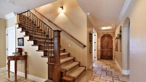 A wooden staircase with carpeted steps leading to a landing, a door on the left, and a hallway with stone flooring and a wooden door at the end. - PRIVATE POOL 34'x18', 25 Minutes to Zion,  Playset for Kids, 7 bdrm, sleeps 32 (Hurricane)