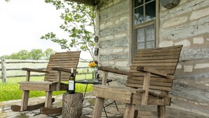 A rustic outdoor seating area with wooden benches and a wine bottle, set against a stone wall and a wooden fence.