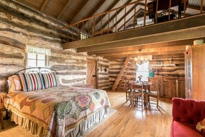 Quarto rústico de cabana de madeira, com uma cama, uma mesa de jantar e uma poltrona vermelha.