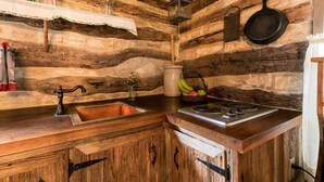 A rustic kitchen with wooden cabinets, a sink, a stove, and a hanging pot rack.