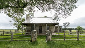 A rustic stone building with a metal roof, surrounded by a wooden fence and lush green grass.