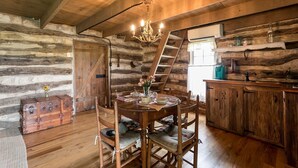 A rustic wooden interior with a dining table, chairs, a chandelier, a ladder, and a kitchen area with a sink and cabinets.