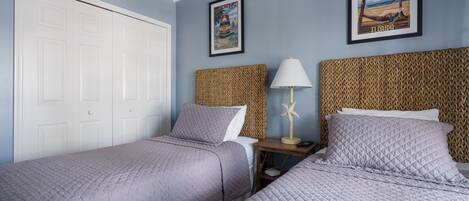 A bedroom with two beds, a white door, a framed picture of Key West, and a woven headboard.