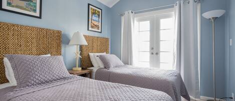 A room with two beds, a ceiling fan, a framed picture on the wall, and a floor lamp.