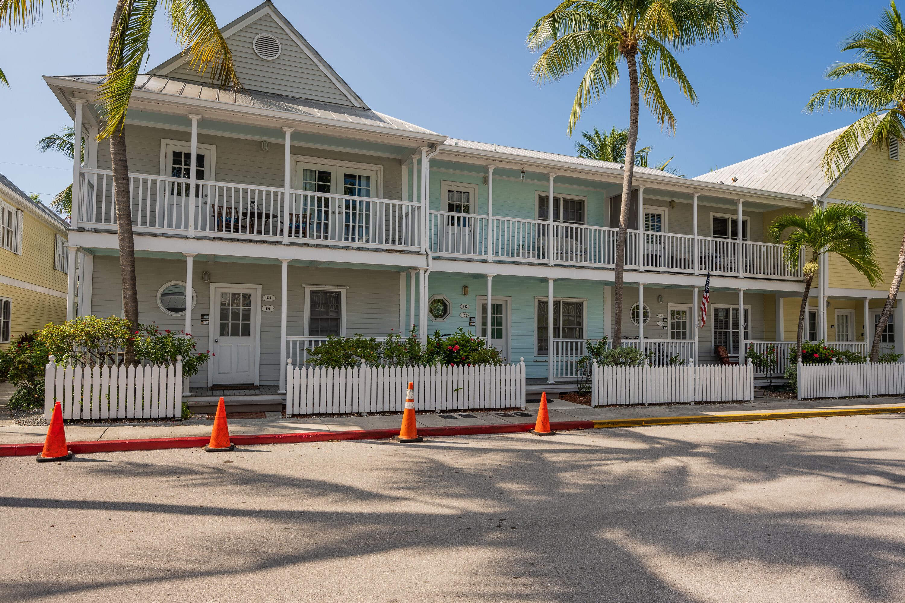 A two-story building with a white picket fence, a balcony on the second floor, and a red curb.
