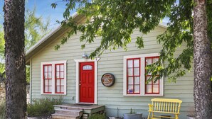 Una casa con puerta y ventanas rojas, un banco y un letrero en la pared.