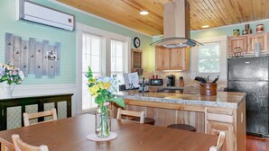 Una cocina con armarios de madera, encimera de granito, refrigerador y un comedor con mesa y sillas de madera.