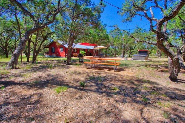 Una casa roja con un porche, rodeada de árboles y una mesa de picnic.