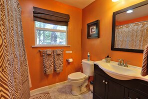 Een badkamer met een oranje muur, een toilet, een wastafel, een spiegel en handdoeken met een patroon.