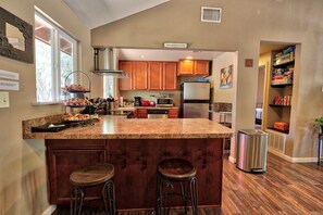Una cocina con gabinetes de madera, encimera de granito, refrigerador de acero inoxidable y horno empotrado.