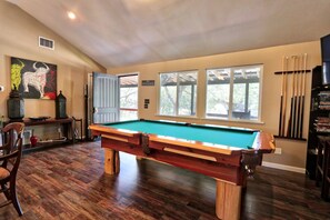 A pool table in a room with wooden flooring, a door leading outside, and a window with a view of trees. - Secluded Cabin with ALL the amenities (Wimberley)