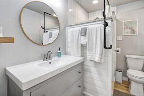 Un baño moderno con un lavamanos blanco, un espejo redondo y un inodoro.