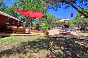 Un espace patio aménagé avec du mobilier d’extérieur, un auvent rouge et un barbecue.