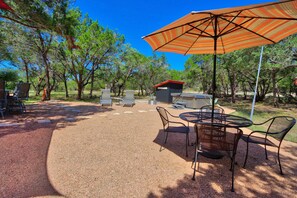 Een terras buiten met een tafel, stoelen, een barbecue en een overdekt gedeelte met een parasol.
