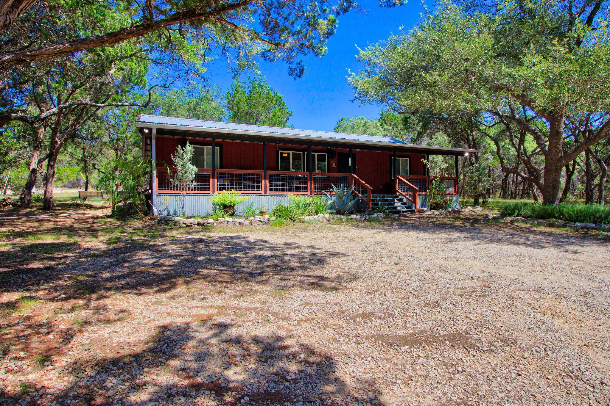 A rustic cabin with a metal roof, surrounded by trees and a gravel driveway.