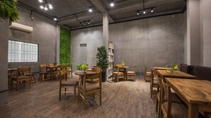Un comedor moderno con mesas y sillas de madera, un muro vertical cubierto de plantas verdes y un amplio ventanal.
