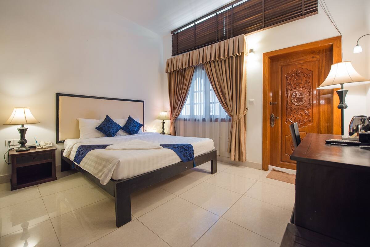 Un dormitorio ordenado con cama, mesitas de noche, escritorio y puerta.