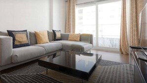 A modern living room with a sectional sofa, a glass coffee table, and a view of the city through large windows.