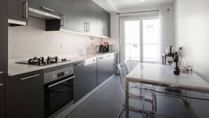 A modern kitchen with grey cabinets, a stainless steel range, and a dining area with a glass table and chairs.