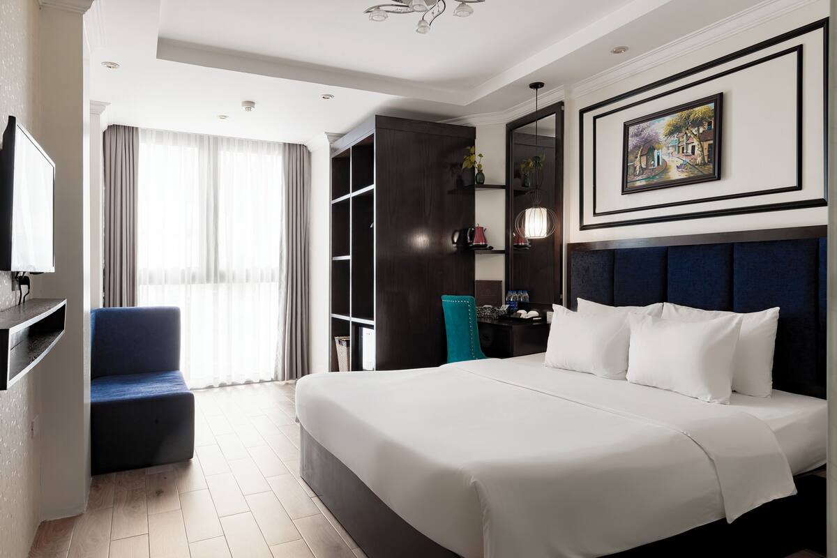 A hotel room with a large bed, a TV, a seating area, and a wardrobe.