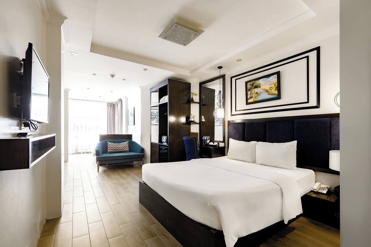 A modern hotel room with a large bed, a desk, a chair, and a TV.