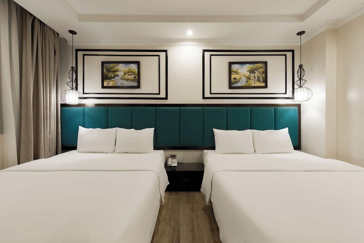 A hotel room with two beds, a teal headboard, a nightstand with a phone, and framed artwork on the wall.