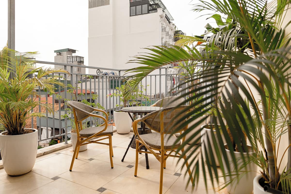 A balcony with wicker chairs and potted plants, overlooking a cityscape.