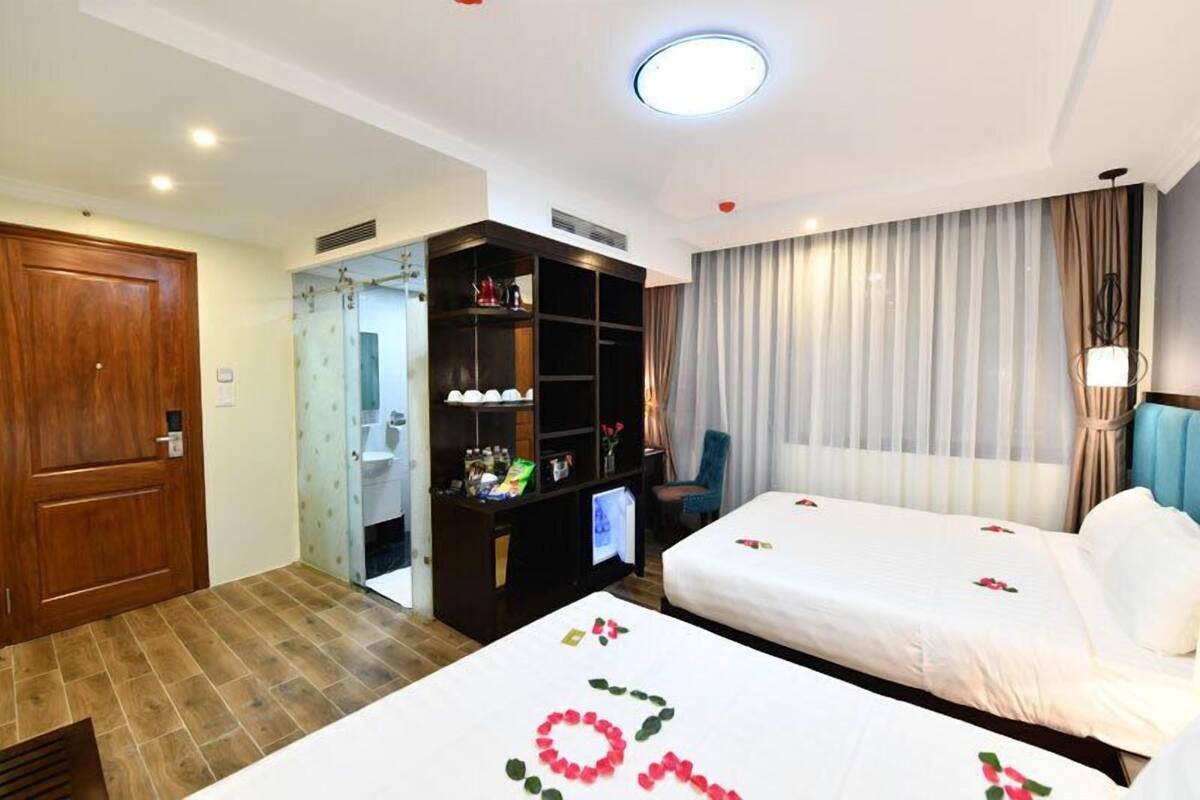 A hotel room with two beds, a wardrobe, a desk with a computer, and a bathroom visible through an open door.