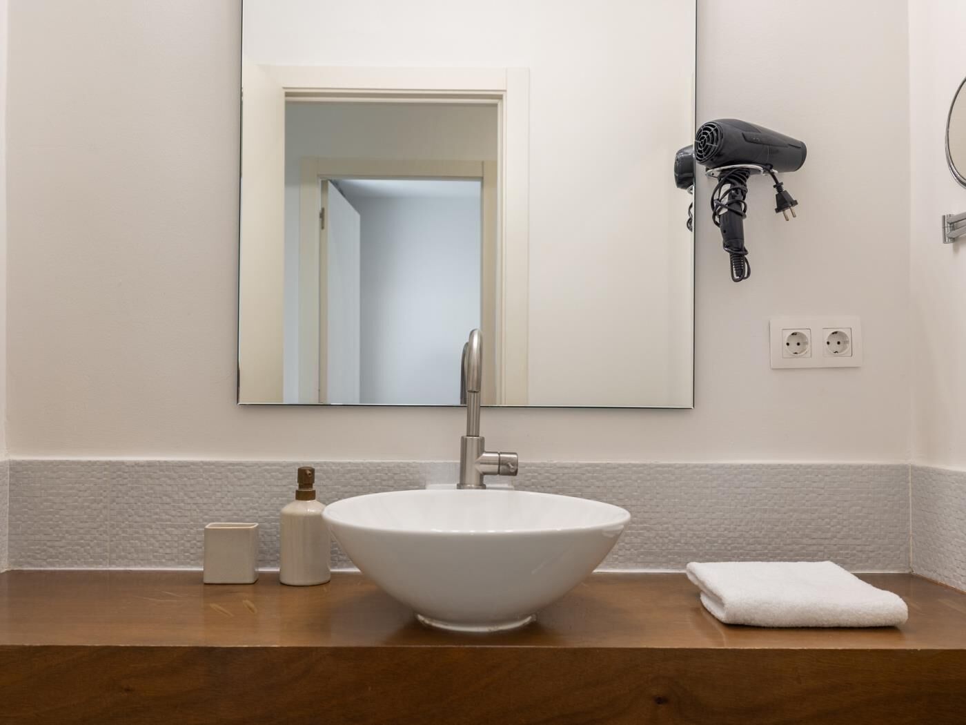 Ein Badezimmer mit einem weißen Waschbecken, einem Spiegel, einem Fön und einem Handtuch auf der Ablagefläche.