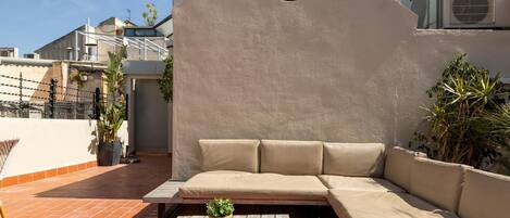 A rooftop terrace with a beige sofa, a wooden table, and potted plants.